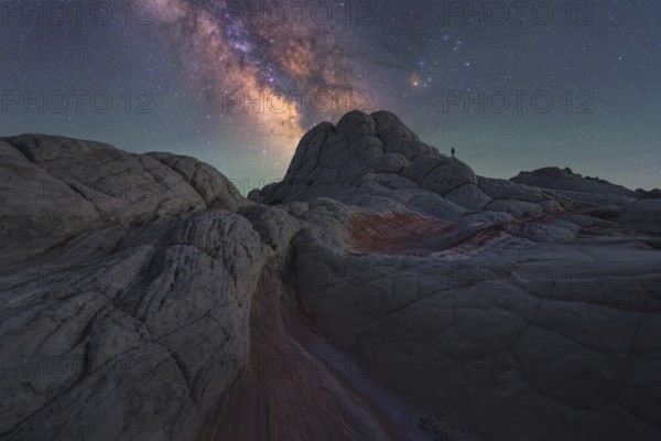 A lone man stands under the majestic Milky Way galaxy in the surreal, alien-like landscape of White Pocket, Arizona, showcasing the cosmic beauty of the night sky