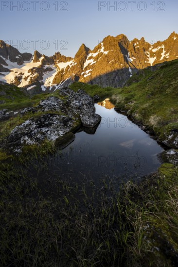 Rocky mountain peaks with reflection, small pond in moor landscape at Trollfjord Hytta, mountain landscape with alpenglow at sunrise, at Trollfjord, Lofoten and Vesterålen, Nordland, Norway