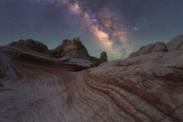 Experience the breathtaking Milky Way shining over the unique rock formations of White Pocket in Arizona's desert. This stunning nightscape captures the serene beauty of the cosmos