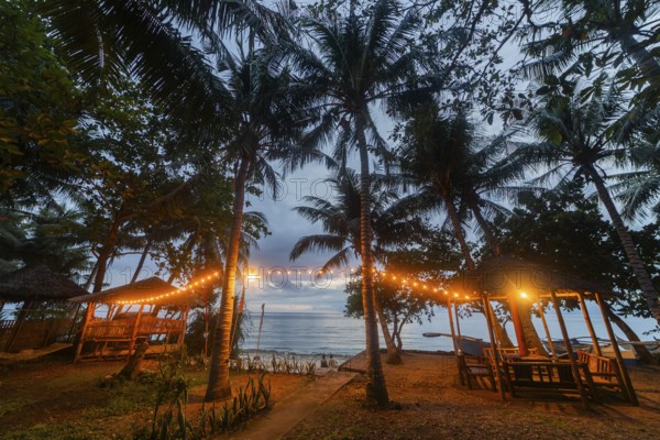 A serene beach view in the Philippines with bamboo huts lit by warm lights at twilight, showcasing the peaceful ambience and romantic setting