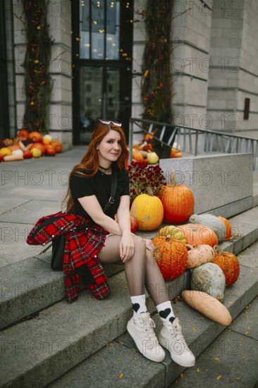 A young woman in autumnal attire sits on stone steps adorned with pumpkins in an urban Montreal setting, capturing the essence of fall with vibrant seasonal decor