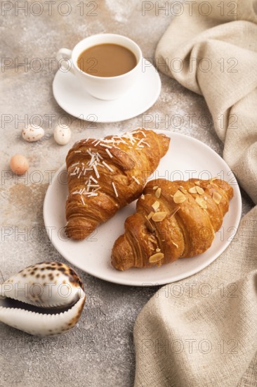 Croissant on white plate on brown concrete background and linen textile, cup of coffee, side view, close up