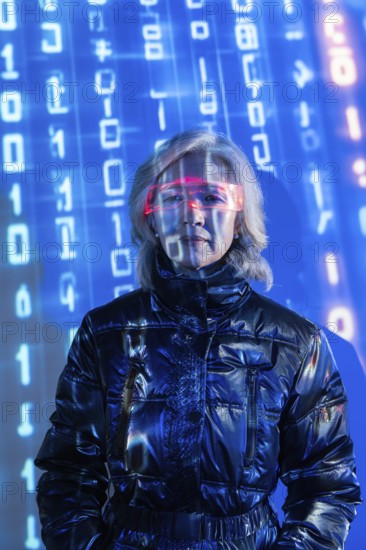 An elderly Asian woman wearing futuristic eyewear is immersed in the metaverse. Blue digital code surrounds her, symbolizing virtual reality and technological advancement