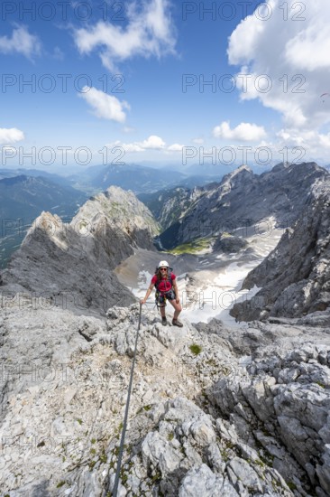 Mountaineer with helmet in a secured via ferrata, Zugspitze via ferrata, ascent to the Zugspitze, view of mountain basin with snow field of the Höllentalferner and Höllental, Wetterstein range, Wetterstein range, Bavaria, Germany