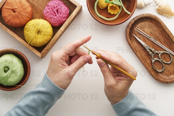 Top view of cropped unrecognizable hands of a woman crocheting in her studio. Surrounded by colorful yarn and crochet tools, she crafts intricate handmade designs
