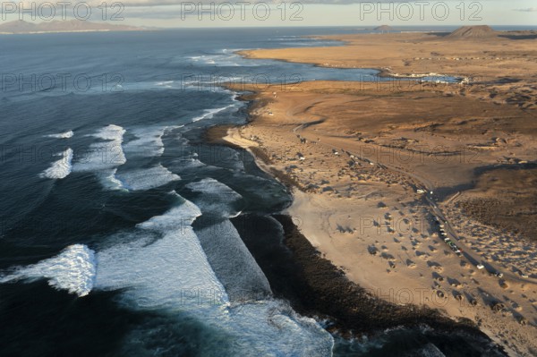 High-angle shot capturing the unique wave patterns and the sandy shore of Popcorn Beach in Fuerteventura, highlighted by the soft evening light