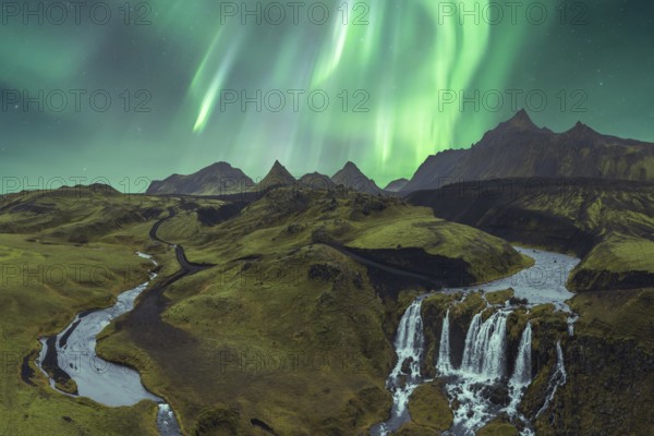 The breathtaking Northern Lights illuminate Iceland's dramatic terrain, featuring stunning mountains, waterfalls, and winding rivers