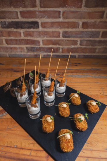 Elegant black slate platter featuring gourmet skewered appetizers in shot glasses with creamy dipping sauce, and crispy bite-sized snacks garnished with microgreens on a rustic table
