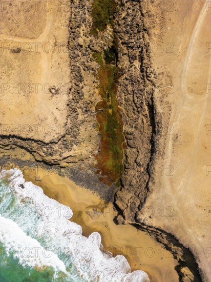 From above, an aerial shot captures a striking natural pool nestled within the rugged coastal landscape of Tindaya Beach in Fuerteventura, Canary Islands
