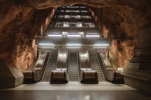 View of escalators at a Stockholm subway station, surrounded by cave-like rock formations. The station design blends urban architecture with natural elements for a unique visual effect