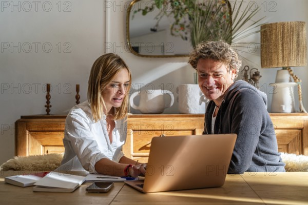 A couple works together at home, focused on a laptop The setting is cozy with a warm atmosphere, featuring a wooden table and modern decor Perfect for remote work themes
