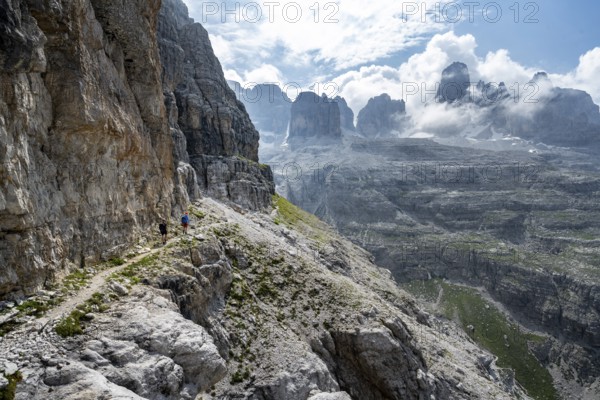 Two mountaineers on a hiking trail in front of a picturesque mountain landscape with rocky peaks, Via Ferrata SOSAT via ferrata, summit of Cima Tosa in the back, Brenta Mountains, Trentino, Italy