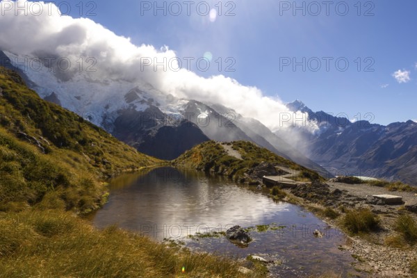 Breathtaking beauty of autumn at Mount Cook, New Zealand. The scene captures the tranquil mountain landscape with lush greenery, dramatic clouds, and a serene waterway