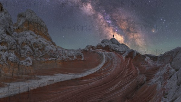 A stunning nightscape of the Milky Way galaxy arching over the unique rock formations at White Pocket in Arizona, US, with a man standing silhouetted against the stars