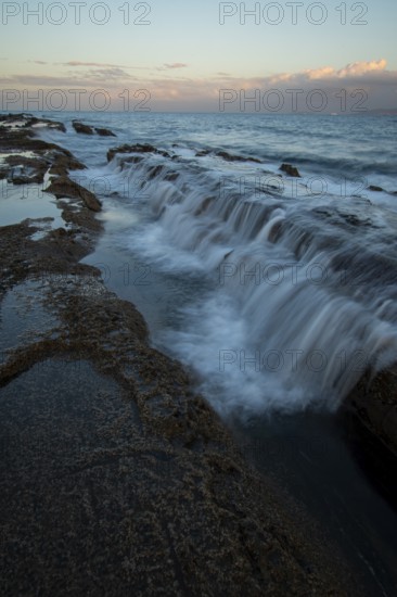 Capturing the serene beauty of a sunset on the rocky shores of Tarifa in Cadiz, where gentle waves meet the coastline under a soft, pastel sky