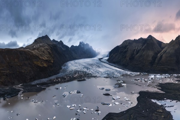 Majestic twilight view of Vatnajökull Glacier, Iceland, with scattered icebergs and dramatic clouded skies over rugged mountains