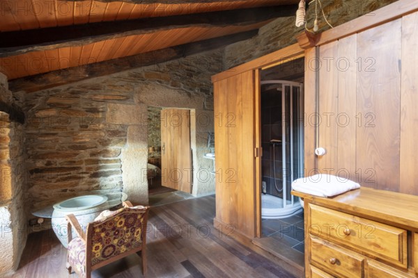 Picture of a charming rustic room inside a country house located in Lugo, Spain, featuring a stone wall, wooden furniture, and a traditional wooden beam ceiling