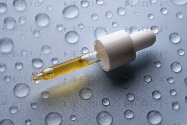 A close-up of a pipette bottle containing vitamin C serum, placed on a surface with scattered water droplets This image highlights the serum's hydrating properties