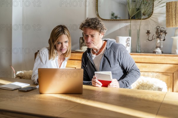 A couple working together at home, engaged with their laptop and notes Sunlight fills the cozy living space, creating a warm and productive environment for remote work