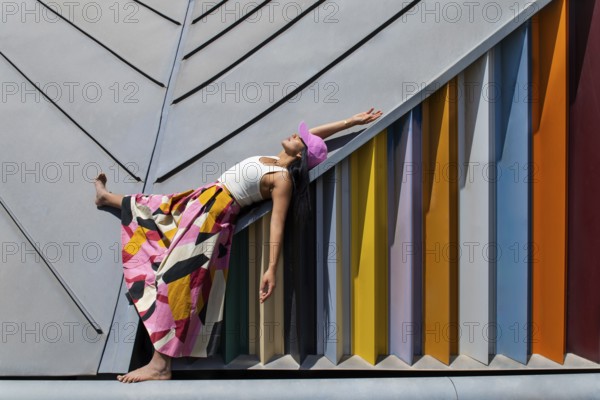 A woman in a vibrant, colorful outfit contrasts strikingly with modern architectural design, creating an eye-catching urban juxtaposition of style and setting