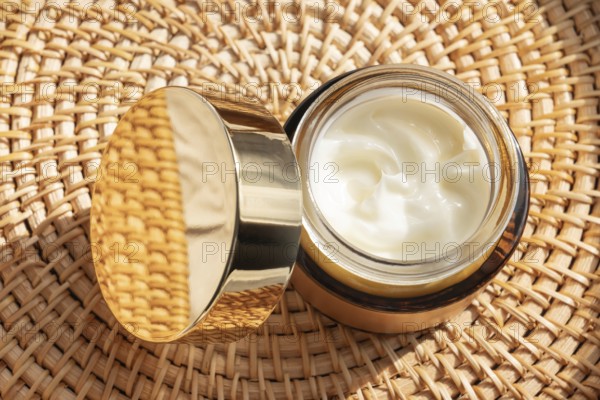 A luxurious skincare cream cosmetic with a golden lid rests on a woven mat. The rich cream inside is highlighted by warm natural light, creating a serene and elegant ambiance