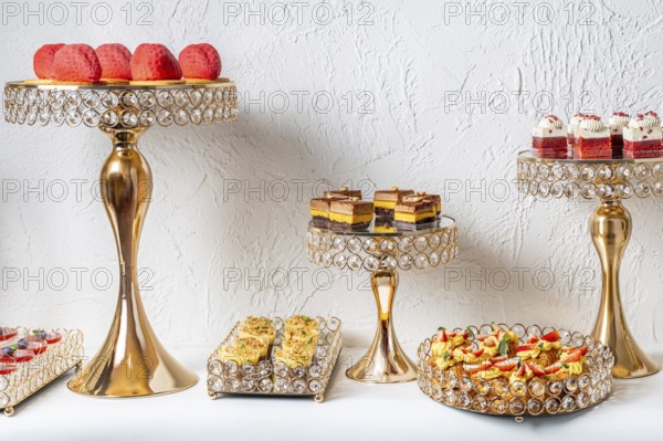 Elegant dessert assortment displayed on luxurious gold and crystal stands. Delicate pastries, cakes, and sweets beautifully arranged on a white background