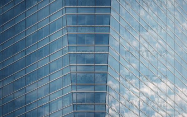 Close-up of a modern glass building facade reflecting a clear blue sky and fluffy clouds, showcasing intricate geometric patterns and lines in a bustling downtown area