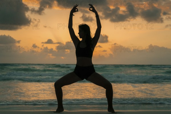 Silhouette of a woman practicing yoga on a beach during sunrise in Tulum, Mexico. The serene atmosphere, coupled with the ocean waves, creates a sense of peace and tranquility