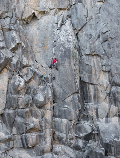 Two climbers scale a rugged cliff with traditional gear, highlighting the thrill and skill of rock climbing in a stunning natural environment. Experience adventure in the wild