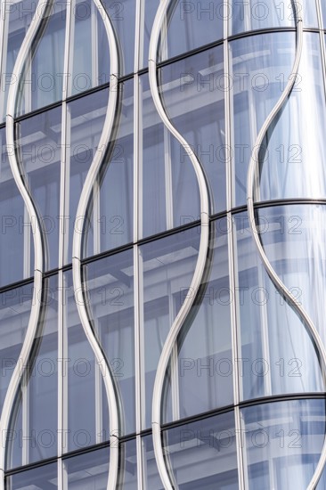 Close-up of a modern building facade, showcasing wavy glass panels and sleek metal frames. The undulating design creates a dynamic and futuristic architectural detail