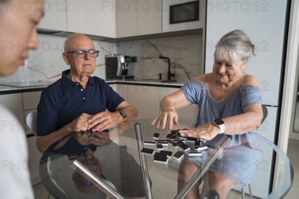 A multigenerational family gathers around a kitchen table, enjoying a lively game of dominoes. Laughter and conversation fill the air, creating heartwarming memories