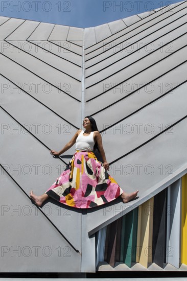 A woman wearing a vibrant, colorful outfit poses against striking modern architecture, showcasing a captivating contrast of urban design and fashion creativity