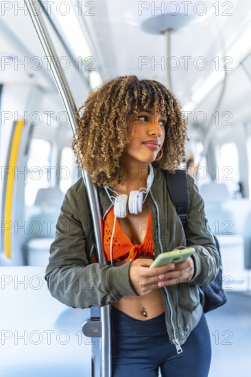 Vertical portrait of a beauty confident latin woman with curly hair and casual clothes using phone standing on the train