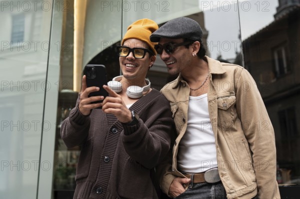 A joyful gay couple shares a moment of laughter while looking at a smartphone. They stand together outside, dressed casually, radiating happiness and companionship