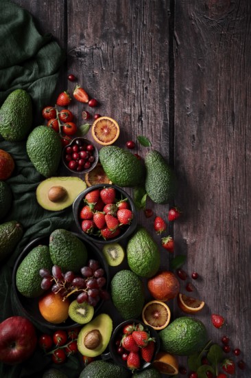 A vibrant assortment of fresh fruits and vegetables, including avocados, strawberries, grapes, and citrus, artfully arranged on a rustic dark wooden table. Perfect for a healthy lifestyle