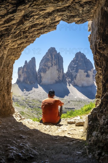 Hiker admiring the tre cime di lavaredo from inside a mountain Tre Cime Cave during a sunny summer day in the italian dolomites