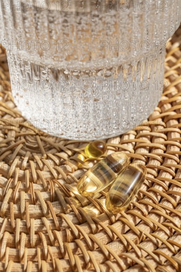 Close-up view of Omega 3 fish oil and vitamin D3 capsules on a woven rattan tray alongside a glass of water, highlighting a healthy lifestyle choice