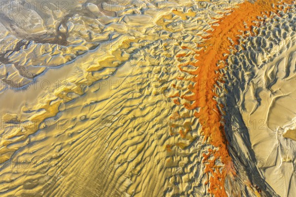 Aerial image showcasing striking orange and yellow sand patterns resembling waves on a beach, creating a mesmerizing natural abstract art. Ideal for backgrounds or nature themes