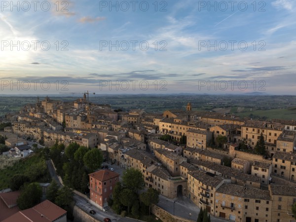 Aerial view of the historic town of Treia in Italy at sunset. The ancient architecture and warm hues create a picturesque scene against the vast countryside backdrop