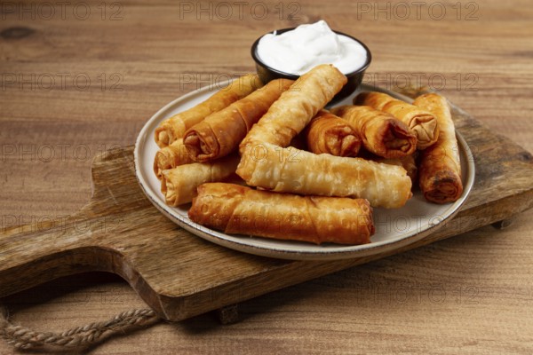 Fried spring rolls with cheese, on a wooden background, with cream sauce, no people