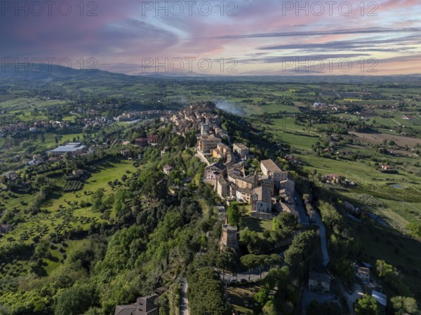 Aerial view of Treia, Italy, capturing the historic architecture and lush countryside under a vibrant sunset sky. A perfect blend of nature and history