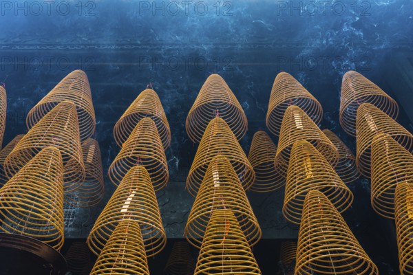 Numerous large, spiral incense coils hanging in a Taoist and Chinese Buddhist temple in Macau, emitting smoke, used during religious rituals