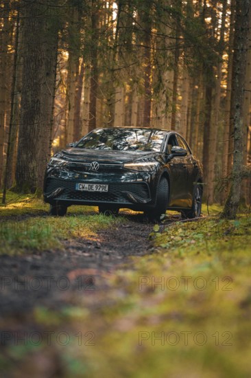 Car on a forest path with grass and light, flanked by tall trees, car sharing vehicle Deer Mobility, electric car VW ID5, Black Forest, Germany
