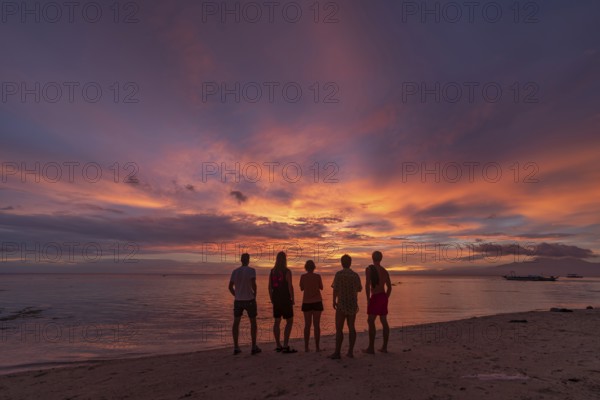 Back view silhouette of unrecognizable friends standing on a beach in the Philippines, watching a stunning sunset with vibrant colors in the sky. Ideal for depicting vacation or holiday scenes
