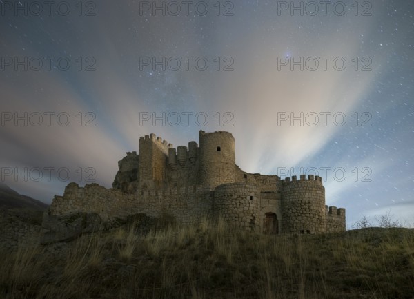 Night falls over the Manqueospese Castle in Avila, Spain, with star trails shimmering above its ancient stone walls