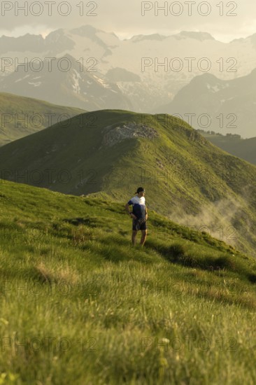 A man pauses to rest on a stunning mountain trail, surrounded by lush green hills under a serene sky, highlighting the harmony of outdoor adventure and nature