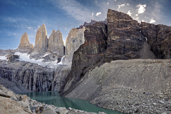 Massive rock formations and snow surround a narrow mountain lake, The rock towers of Torres del Paine in Patagonia Chile