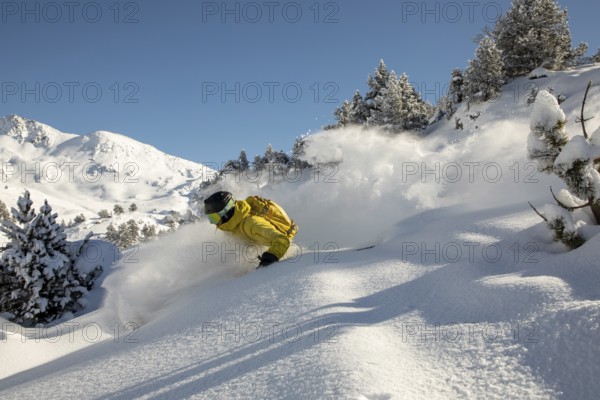 Dynamic freeride skiing in fresh powder snow with a skier in a yellow jacket navigating through a beautiful mountain landscape under a clear blue sky, capturing the thrill and excitement