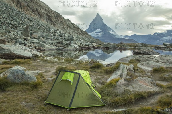 A vibrant green tent is set by a tranquil alpine lake, with the majestic Matterhorn towering in the background, showcasing Zermatt's stunning summer scenery in Switzerland