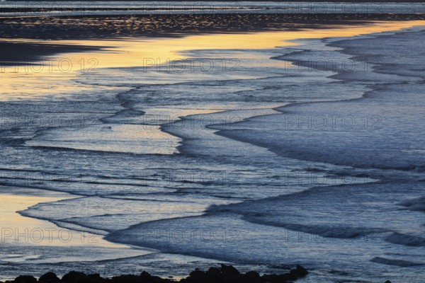Low tide and gentle waves, at dusk on the North Sea, on the North-east coast of Northumberland, England, UK
